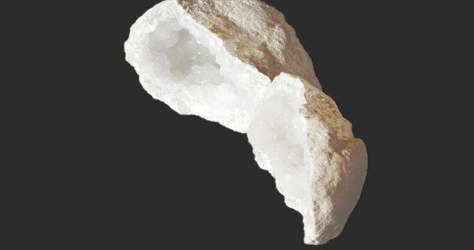 Split white geode rotating on a dark gray background, revealing a sparkling crystal-lined interior and rough natural outer surface.