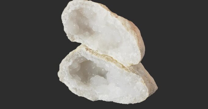 Two halves of a white geode rotating on a dark gray background, showing sparkling crystal-lined cavities and the rough natural exterior.