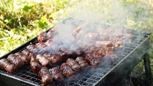 Cevapi cook on a hot charcoal grill as thick smoke rises outdoors. Traditional Balkan barbecue footage fits food, travel, summer and hospitality themes