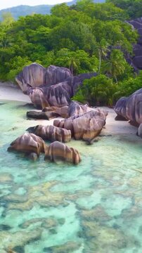 Vertical aerial orbit over Anse Source d'Argent in Seychelles revealing turquoise water, white sand, granite rock formations and lush tropical coastline.