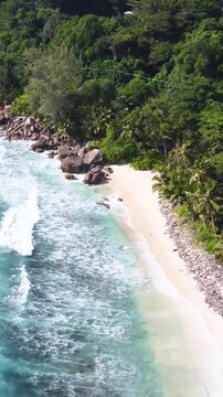 Vertical aerial orbit over Anse Takamaka in Seychelles showing turquoise water, white sand, granite rocks and lush tropical coastline.