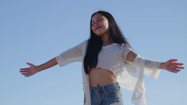 Happy woman on beach during meditation enjoying breathing fresh air, standing with open arms under blue sky while feeling freedom and happiness during summer vacation travel.