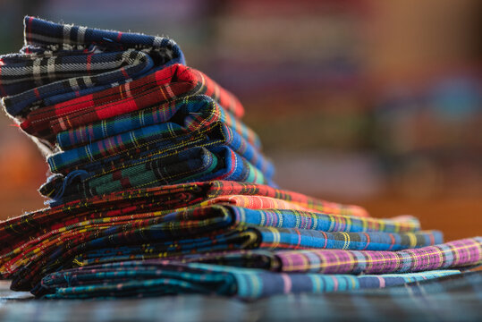 Colorful textile stack of vibrant fabric with detailed weave and pattern checkered samples in warehouse. Close up of bright plaid folded cloth and pile of fabric with traditional design.
