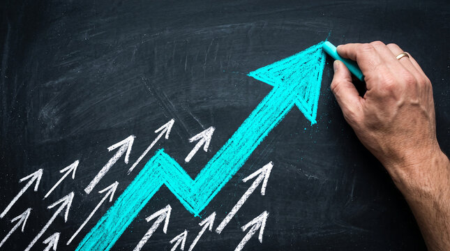 A hand draws a vibrant turquoise arrow on a chalky black surface, symbolizing growth and success. Representative of business progress, strategy, and achievement.