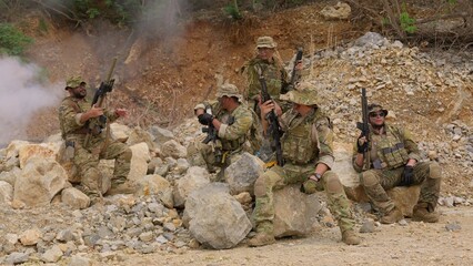Naklejka premium An elite team of special forces soldiers in full tactical gear pose together with their rifles amidst smoke and rocks during a military operation in a rugged combat zone.