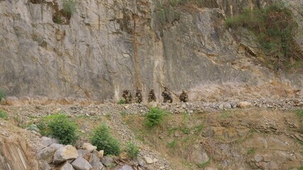 Fototapeta premium A military squad in camouflage takes a tactical position with rifles during a mission on a rugged cliffside, demonstrating teamwork and battlefield vigilance.