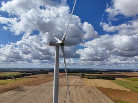 Vue a&eacute;rienne d'une &eacute;olienne &agrave; la campagne, au milieu des champs et des cultures agricoles avec un ciel bleu et des petits nuages cumulus blancs. France 2026