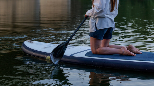 Woman kneeling on paddleboard holding paddle on calm water surface