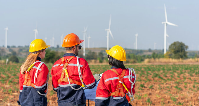 Team workers training wind turbine power generator sustainability performance brainstorming together at Renewable Energy Plant Back view of three engineers holding blueprint inspecting windmill