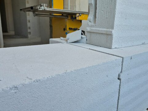 Close-up of aerated autoclaved concrete blocks with a block cutting bandsaw machine in the background.