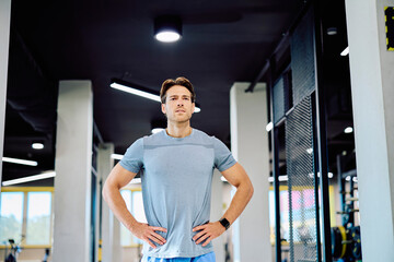 Naklejka premium Athletic man standing with hands on hips, looking focused and determined during a workout session at a contemporary gym