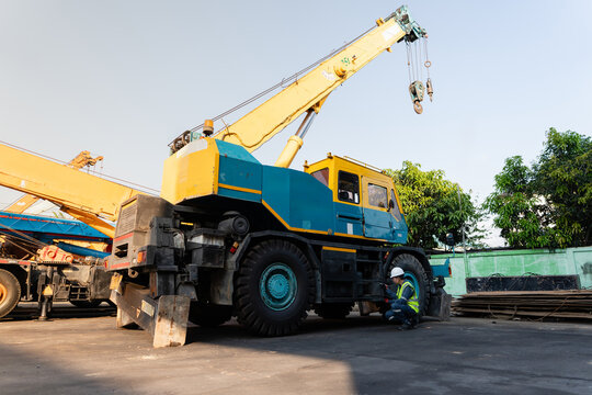 Male safety engineer reviews lifting operations using a clipboard while kneeling beside the heavy industrial mobile crane