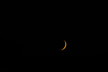 A delicate golden sliver of a crescent moon glowing brightly against the pitch-black canvas of the deep night sky. Minimalist astrophotography with ample copy space for text or graphics © AgioiDouloi