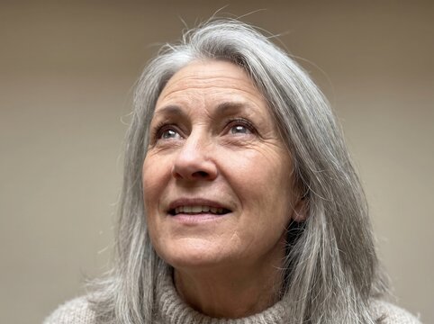 Senior woman with grey hair looking upwards with an expression of hope and wonder