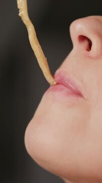 Close up of woman eating noodles focusing on her lips and food. subject repeatedly opens mouth to take bites from thin noodle strands held by hand with soft lighting highlighting skin