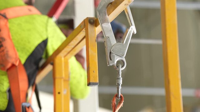 Fall protection lanyard carabiner hook secured on scaffolding rail during structural installation and site safety compliance work