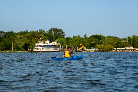 Sea kayaker paddling toward Wards Island with a ferry and crowd in the background on a summer evening in Toronto, with copy space in the sky