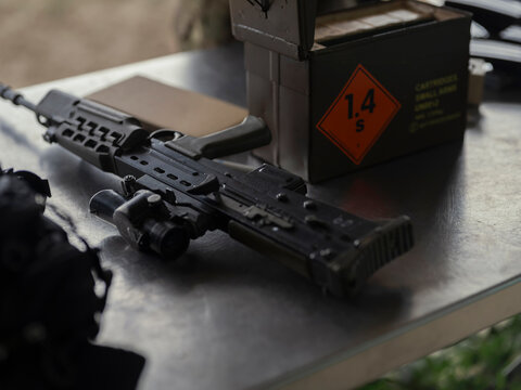 An SA80 rifle on a steel table beside an ammunition box marked with a hazard class label, waiting to be issued on a military range.