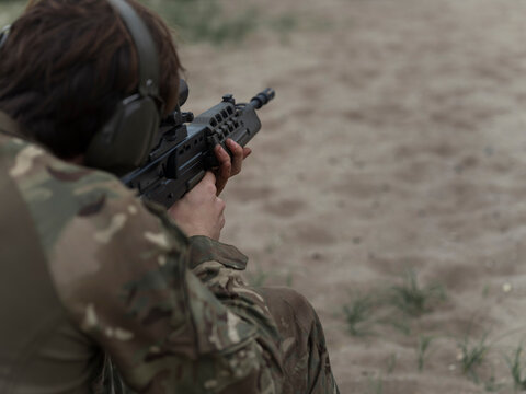 Over the shoulder view of a soldier settled behind an SA80 rifle, hands steady on the handguard as he prepares to fire.