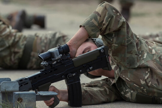 A soldier lies back with head resting on one arm beside a service rifle on the firing point, waiting for the next serial to begin.