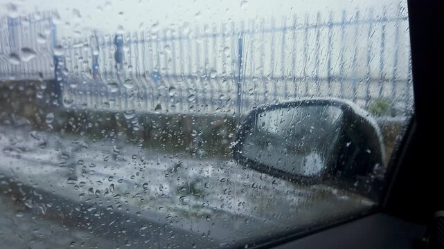 Water droplets on a car side window and mirror during slow motion snowfall on an overcast day