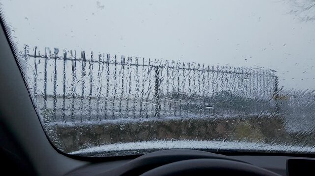 Slow motion snow falling beyond a water covered windshield viewed from inside a car
