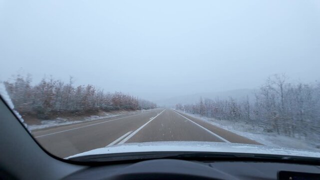 Driving on a snow covered rural highway during active snowfall under an overcast winter sky