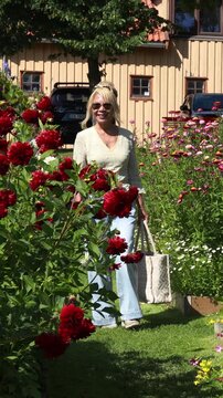 Woman walking in a beautiful blooming flower garden. Vertical design in 9:16 ratio. Smartphone and social media ready.	
