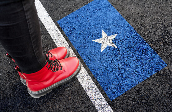 a woman with a boots standing on asphalt next to flag of Somalia and border
