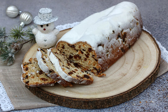 Traditional German Christmas stollen dusted with powdered sugar, sliced and served on a wooden platter with Christmas decorations.