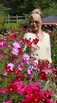 Woman walking in a beautiful blooming flower garden. Vertical design in 9:16 ratio. Smartphone and social media ready.	