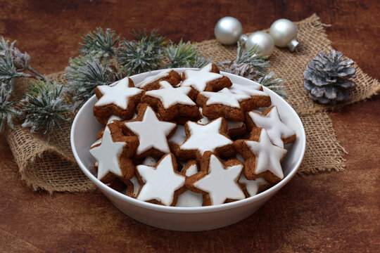  Eine wei&szlig;e Schale mit Zimtsterne auf rustikalem Holzhintergrund mit weihnachtlicher Dekoration.