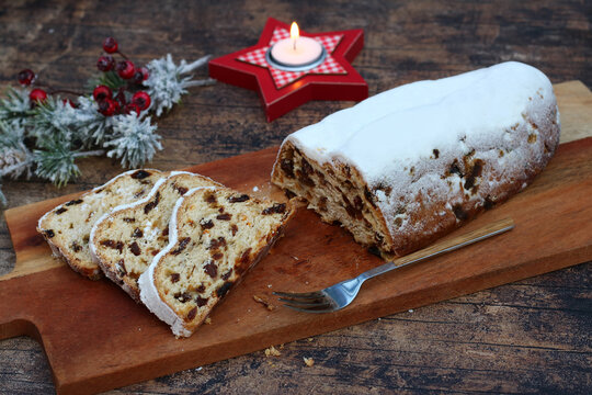 Traditioneller deutscher Christstollen mit Puderzucker, aufgeschnitten auf einem Holzbrett mit Teelicht und weihnachtlicher Dekoration.