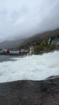 HELLESYLT, NORWAY - OCTOBER 9, 2024: View of the famous Hellesylt waterfall flowing through the village, with the bridge and surrounding buildings in the Norwegian fjords.