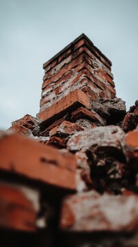 Crumbling old brick chimney closeup with damaged masonry against gray sky