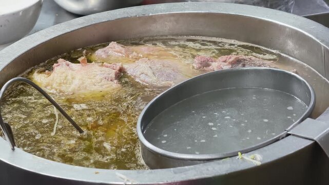 Large pot of boiling beef pho broth with chunks of meat and a strainer ladle at a traditional Vietnamese noodle restaurant