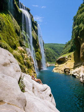 Person relaxes on a rocky ledge near a powerful waterfall