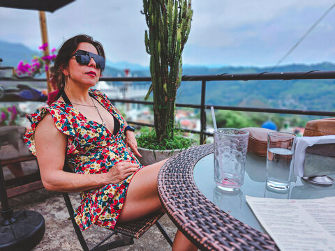 Woman relaxes at a rooftop cafe, sunglasses on, smiling