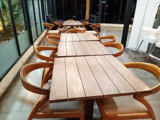 Fotobehang Horeca Empty wooden dining tables and chairs arranged in a cafe interior, ready for guests in a hospitality setting  © Adipra