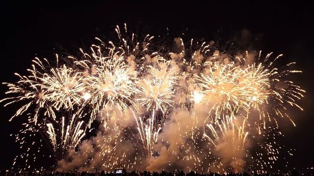 Spectacular fireworks display illuminates night sky with vibrant bursts of light and smoke, celebrating a festive occasion above silhouetted crowd enjoying event.
