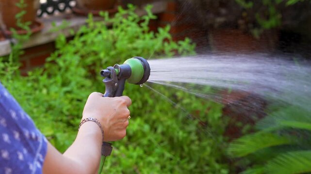 Slow motion close up of woman watering lush garden plants with a handheld hose nozzle