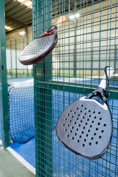 Padel racket hanging on fence beside indoor court