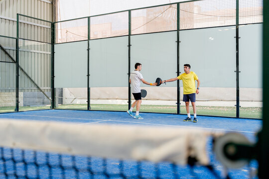 Padel doubles teammates greeting across the net on court