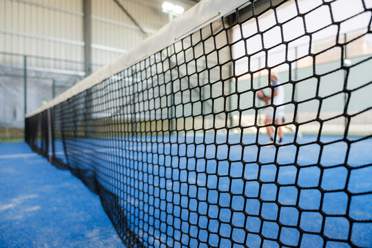 Padel court net close-up with player in indoor arena