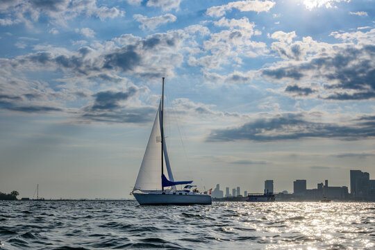 Sailboat crossing Toronto's Inner Harbour with sunlight glinting off the water under dramatic clouds on an August evening
