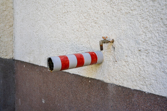 A red and white striped pipe protruding from a textured wall next to a small metal water faucet