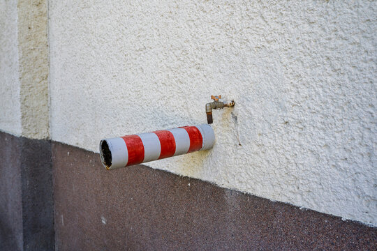 A metal water faucet attached to a textured wall with a red and white striped pipe extension