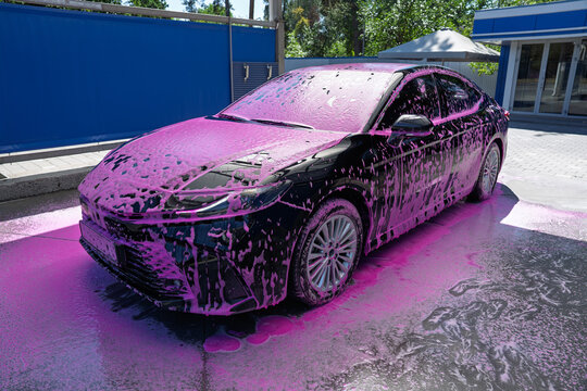 Black car covered in pink foam at a self service car wash station