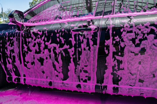 Black car covered in pink foam during a professional car wash service