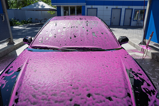 Car covered in pink active foam at a self service car wash station